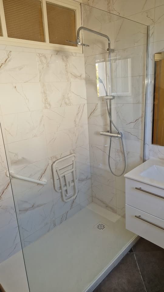 Après : douche à paroi vitrée, carrelage effet marbre, siège rabattable et barre d’appui