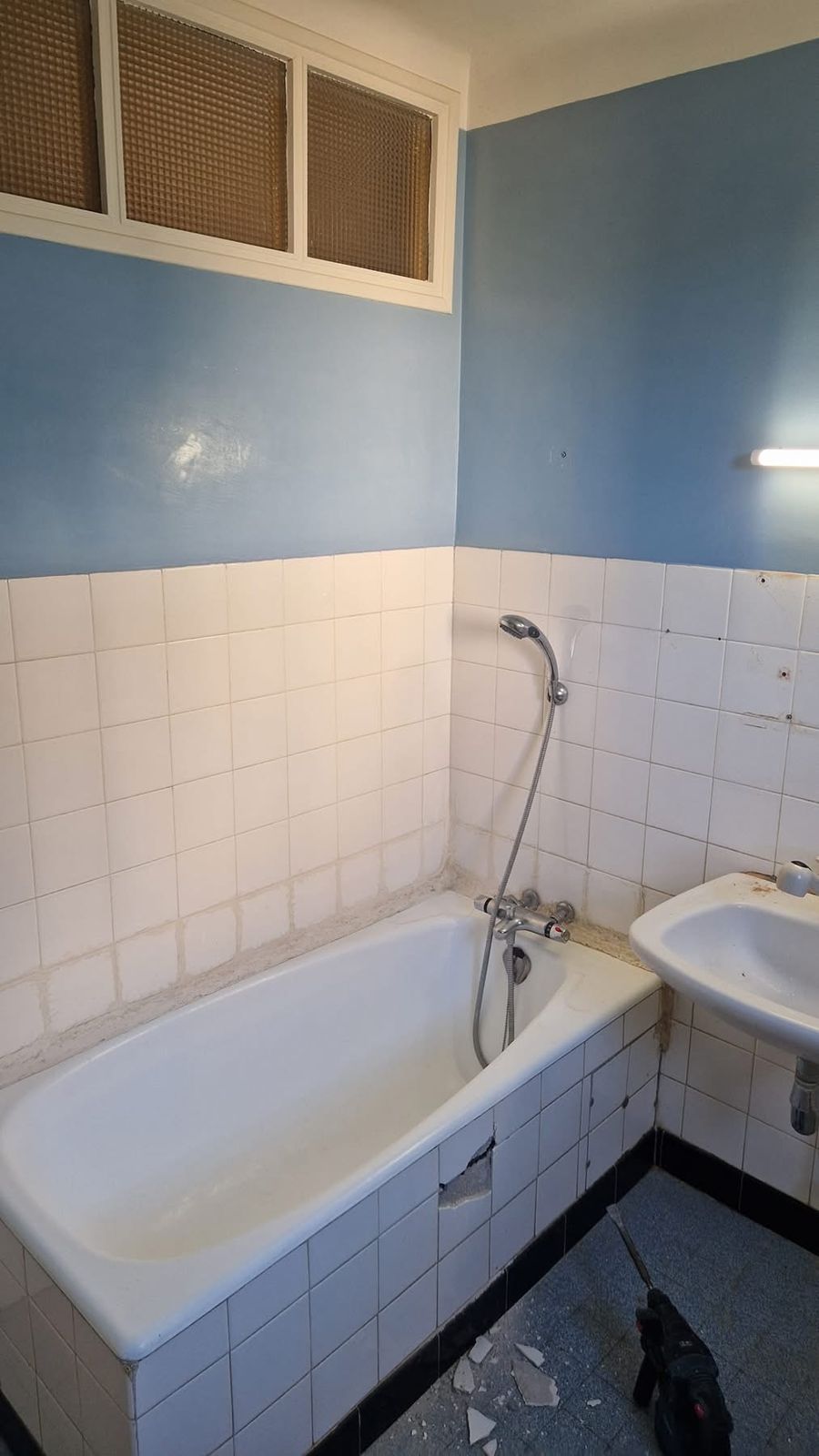 Avant : salle de bain avec ancienne baignoire, faïence blanche abîmée et murs bleus