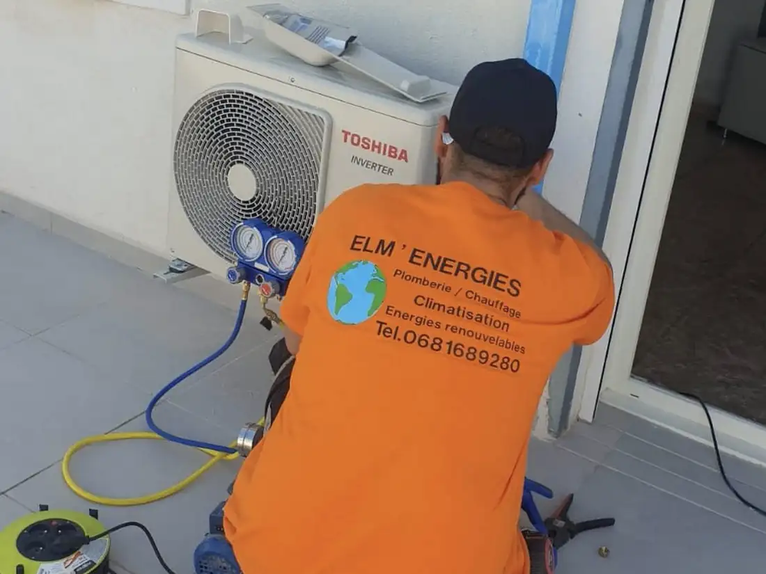 Technicien d’ELM’ Énergies en t-shirt orange, manomètres branchés sur une unité extérieure de climatisation Toshiba