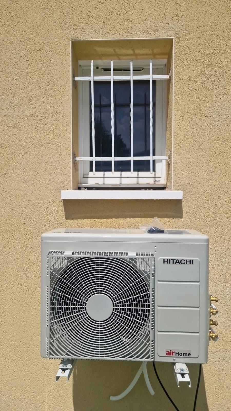 Unité extérieure de pompe à chaleur Hitachi fixée sur une façade, sous une fenêtre à barreaux