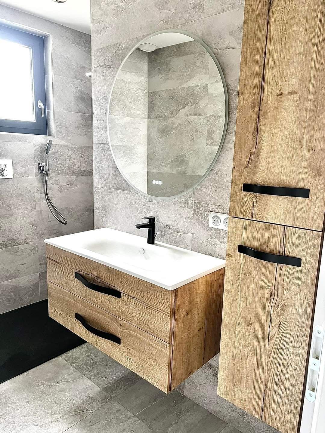 Salle de bain avec meuble vasque suspendu en bois, colonne assortie, miroir rond lumineux et douche